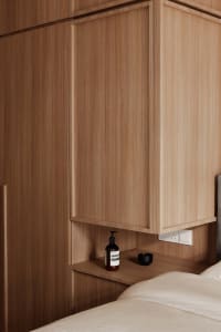 A modern bedroom featuring a wooden cupboard with built-in shelves and a black bottle of lotion.