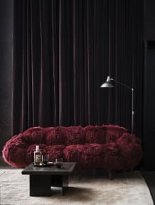 A modern living room featuring a plush, burgundy velvet couch, a black coffee table with a whiskey bottle and glasses, and a 