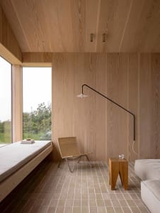 A minimalist living room featuring wood-paneled walls and a window seat with a wicker chair.