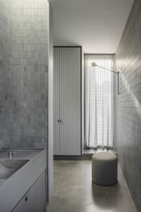 A modern bathroom featuring concrete-tiled walls and flooring, with a concrete sink and minimalist design elements.