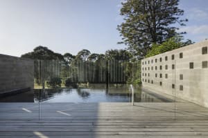 A modern outdoor pool with a cement concrete structure and glass dividers, surrounded by trees and greenery.
