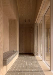 A modern wooden hallway with a tiled floor and a floating concrete bench.