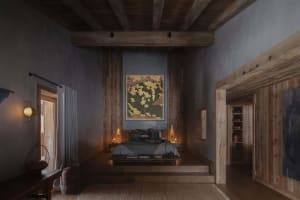 A minimalist bedroom with dark walls, wooden floors, and a botanical painting hanging above the bed.