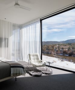 Modern minimalist bedroom featuring a white leather chair with a glass window overlooking mountains and a river.