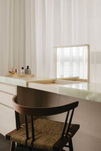 A minimalist vanity with a marble countertop and a wooden chair with a woven seat.