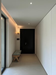 Minimalist interior design featuring a bench with a cushion and a black door in a concrete hallway