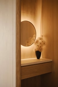 A minimalist interior design with light-colored wooden walls and a round mirror with illuminated lighting.