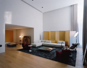 A minimalist living room with a white sofa, red armchairs, and wooden floor.