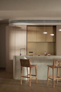 Modern, minimalist residential kitchen with concrete countertops and wooden stools.