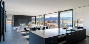 Modern kitchen featuring a large island with a metallic countertop, glass windows overlooking mountains, and a minimalist des