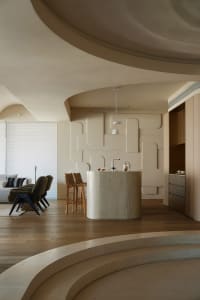 Modern residential kitchen featuring a circular bar with a concrete finish, barstools, and minimalist design elements.