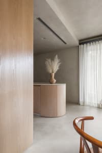 A minimalist living room with wooden furniture and a vase of dried plants.
