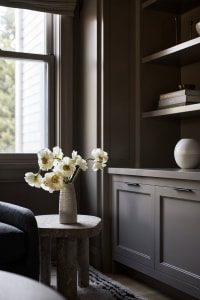 A modern living room with a grey concrete cabinet featuring white flowers in a vase.