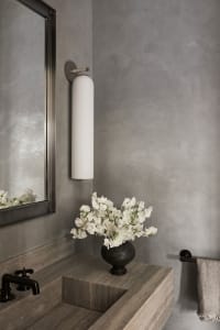 A modern, minimalist bathroom featuring concrete walls and a floating sink, with a vase of white flowers adding a touch of na