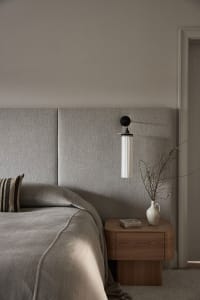 Minimalist bedroom featuring a grey upholstered bed and wooden nightstand with a vase and plant.
