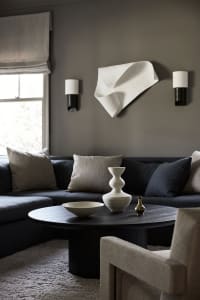 Minimalist living room featuring a textured fabric couch, modern coffee table with decorative vases, and abstract wall art.