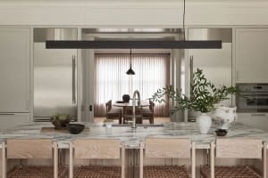 Contemporary residential kitchen featuring marble countertops, wooden chairs, and steel appliances.