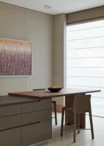 Modern, minimalist kitchen featuring wood cabinets and a wooden dining table with a bowl of oranges.