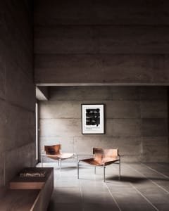 A minimalist modern living room with concrete walls, leather furniture, and a framed artwork.