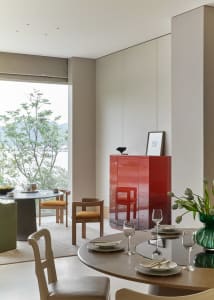 A modern minimalist dining room with a circular table, chairs, and a red cabinet.