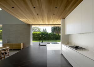 Modern residential kitchen featuring concrete countertops, wood cabinetry, and a view of the outdoor area with greenery and a