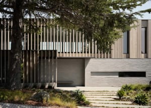 Modern exterior of a residential house featuring a wood cladding on the upper floor, with a minimalist driveway and landscapi