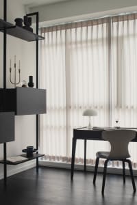 A modern, minimalist home office featuring a sleek desk, chair, and shelving unit with neutral colors and a large window with
