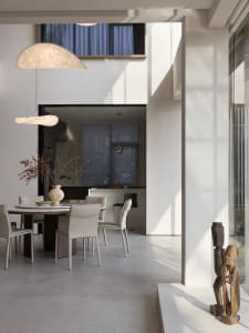 Modern dining room with a round table, white chairs, and a vase of dried flowers on the table, with a kitchen area in the bac