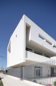 A modern building with a white concrete exterior, featuring a minimalistic design with large windows and a flat roof.