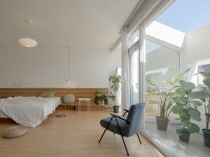 A minimalist modern bedroom featuring a wood floor, white bed, and large window.