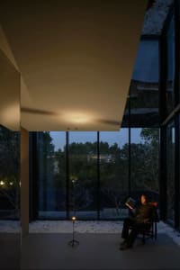 A modern interior design featuring a glass window with a person reading a book at dusk.