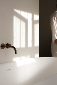 A modern bathroom featuring a freestanding tub made of ceramic material, with sunlight casting shadows onto the wall from a w