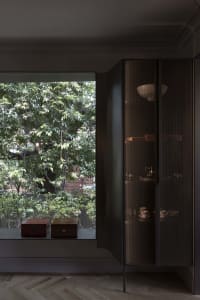 A modern interior design featuring a glass cabinet with a metal mesh door and wooden boxes on the windowsill.