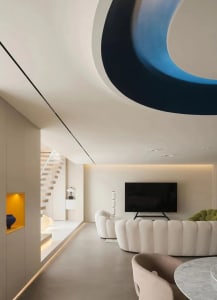 A modern living room with a curvilinear blue ceiling feature and concrete floor.