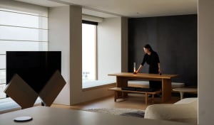 Person arranging a candle on a wooden table in a minimalist living room with oak and black materials.