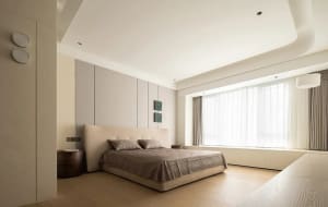 A minimalist modern bedroom featuring a beige bed with matching beige bedding and curtains.