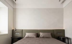 A minimalist bedroom with a beige bed, grey headboard, and pendant lights.