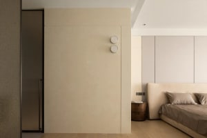 Neutral-toned minimalist bedroom featuring a large bed, side table, and minimalist wall panels.