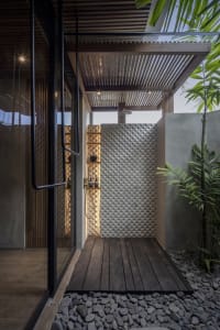 An industrial outdoor shower area with concrete walls and a wooden deck surrounded by rocks and plants.