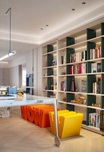 A modern living room featuring a library area with books on shelves, colorful yellow and orange stools with the word 'WOW', a