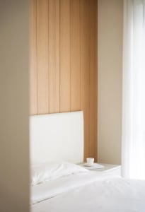 A minimalist bedroom featuring white furniture and wood paneling.