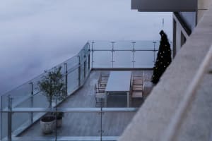 Modern rooftop balcony with glass railings adorned for Christmas, featuring a potted olive tree and a decorated Christmas tre