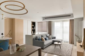 A modern living room with a neutral color palette, featuring a gray sectional sofa, round coffee table, and large windows wit
