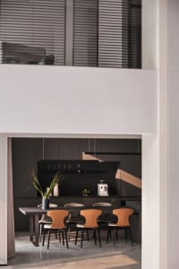 A modern kitchen interior with sleek, minimalist design elements, featuring a dark wooden table, leather and metal chairs, an
