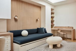 A modern living room with wooden walls, a blue sofa, and a white pouf on a patterned rug.