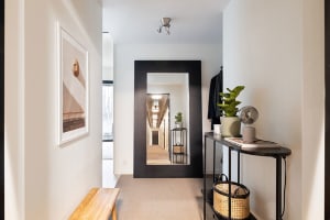 A modern minimalist entrance/hallway showcasing sleek black furnishings and natural light, with a wooden bench and potted pla