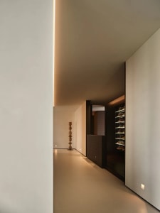 A modern minimalist hallway with concrete walls, floor, and ceiling, featuring a floor lamp and a built-in shoe rack.