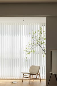 A clean, modern interior design featuring vertical fabric blinds and a minimalist armchair.