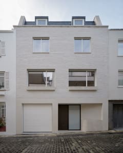 A modern, white-brick residential exterior with brick roofing, large windows, and a garage door.