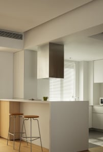 A modern white kitchen features a bar stool counter with two stools.